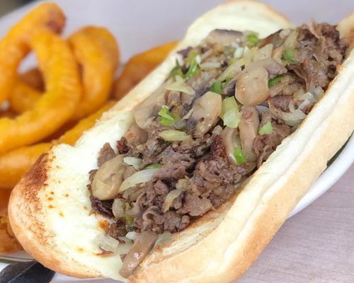 Philly cheesesteak sandwich with onion rings.
