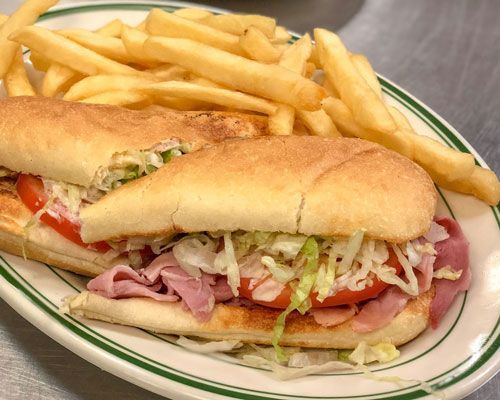 Sub sandwich with ham, tomatoes, lettuce, and fries on a plate.
