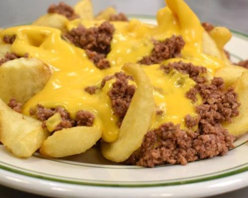 Fries topped with yellow cheese sauce and crumbled brown meat on a white plate.