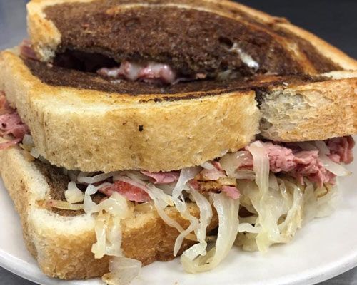 Reuben sandwich with corned beef, sauerkraut, and melted cheese on toasted rye bread.