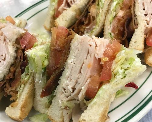Turkey club sandwich on a plate with lettuce, tomato, and bacon.