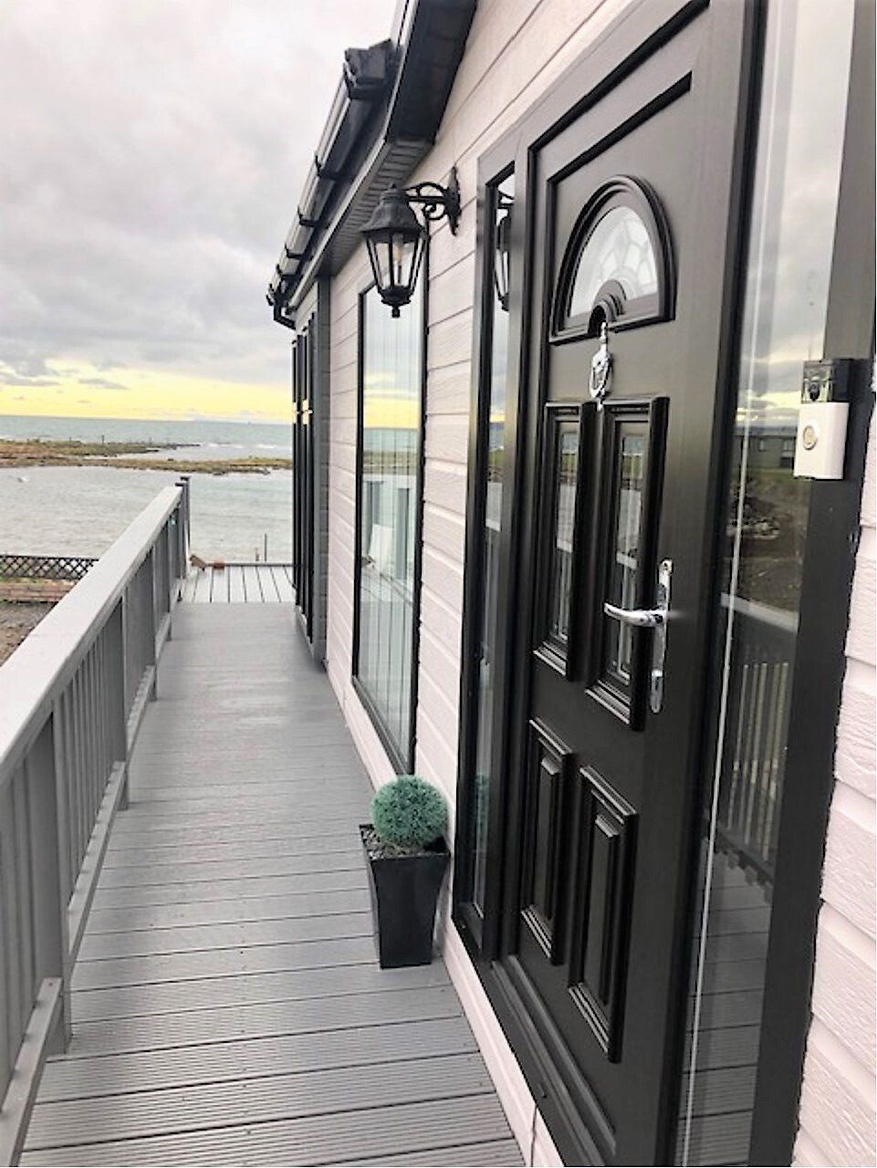 A white house with a black door and a balcony overlooking the ocean.