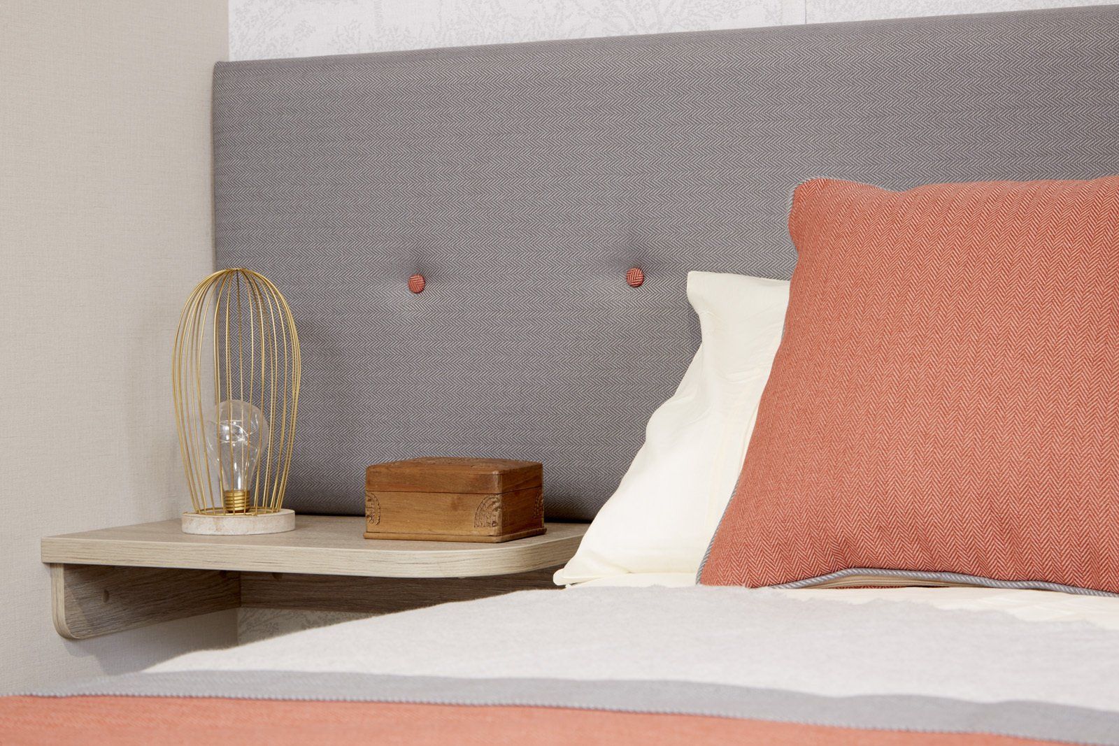 A bed with a gray headboard and a pink pillow on it.