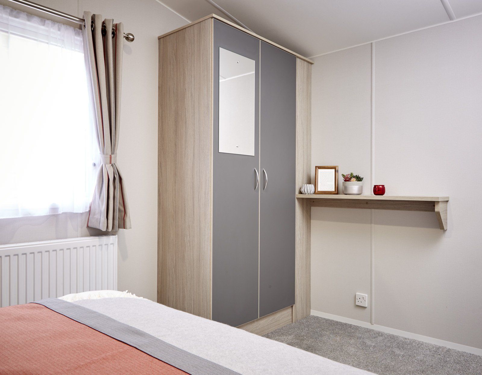 A bedroom with a bed , wardrobe , mirror and shelf.