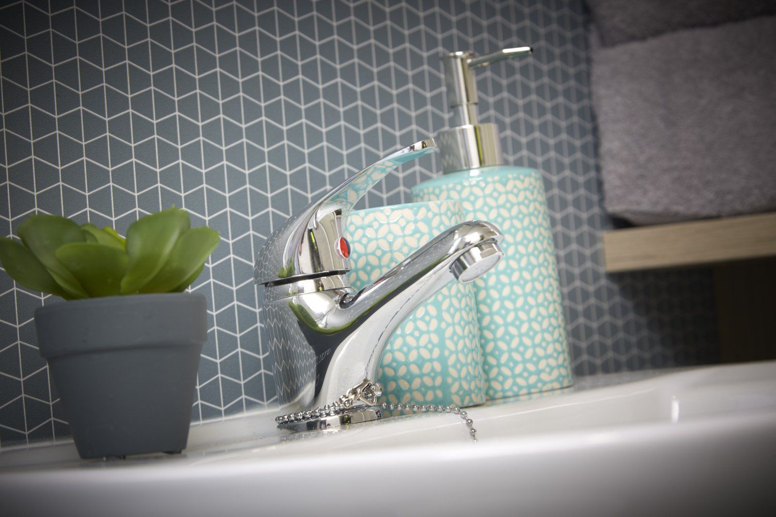 A bathroom sink with a faucet , soap dispenser , and potted plant.