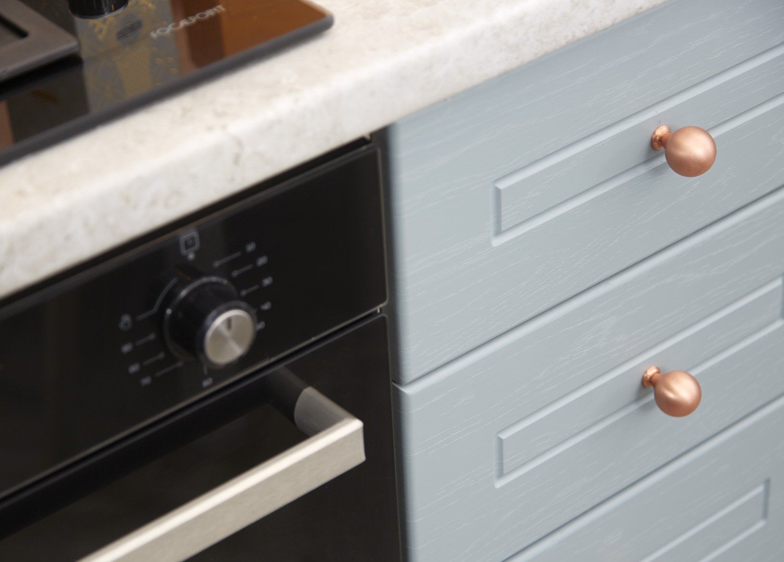 A close up of a black oven and blue cabinets in a kitchen.