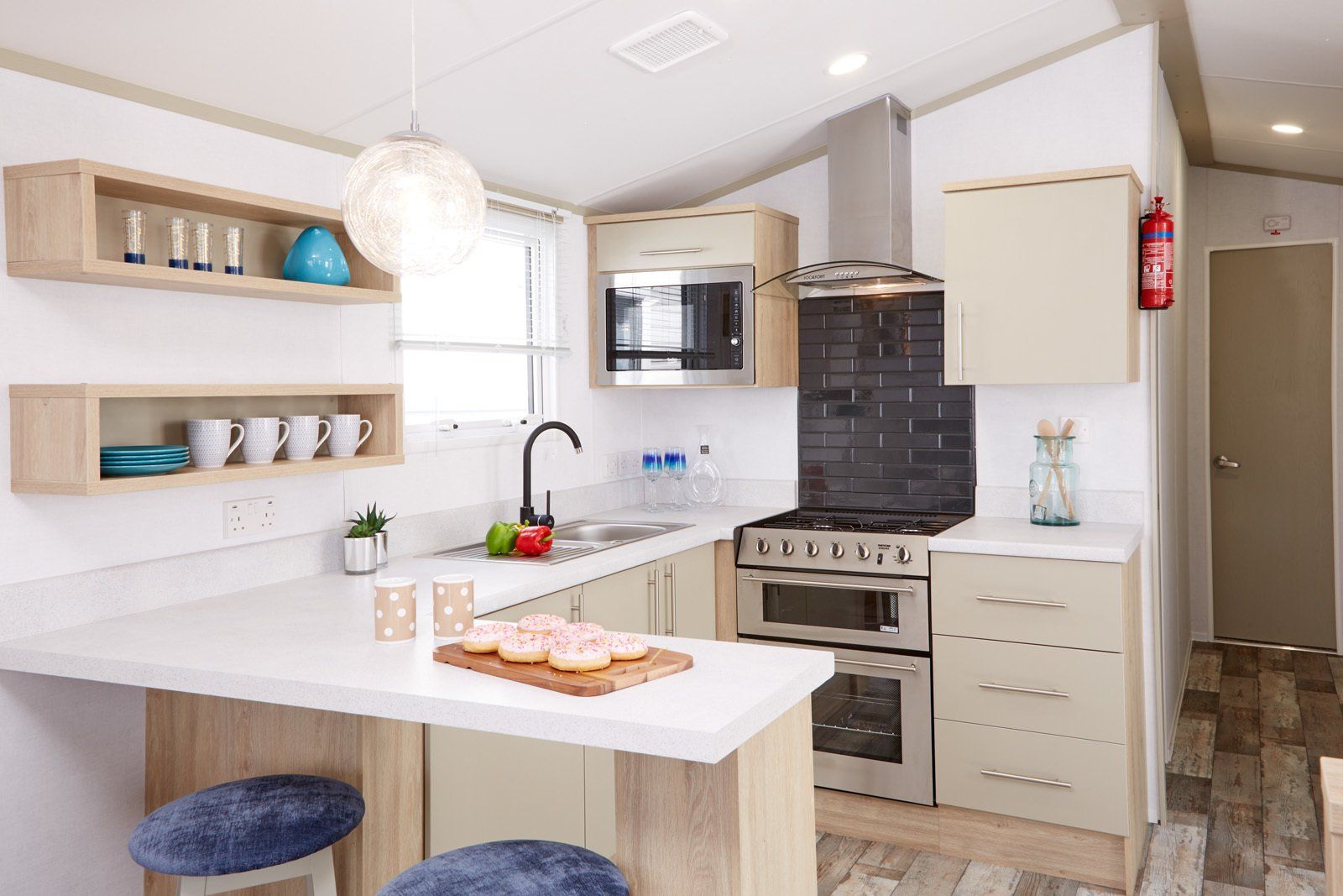 A kitchen in a mobile home with a stove , microwave , sink and stools.