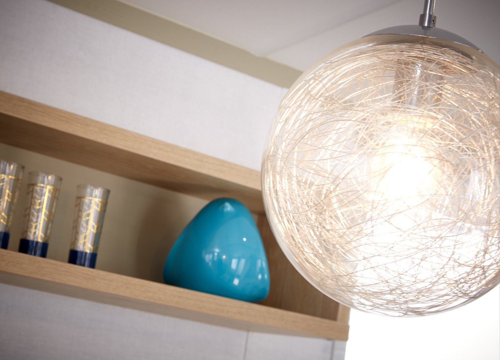 A light hanging from the ceiling next to a shelf with a blue vase on it
