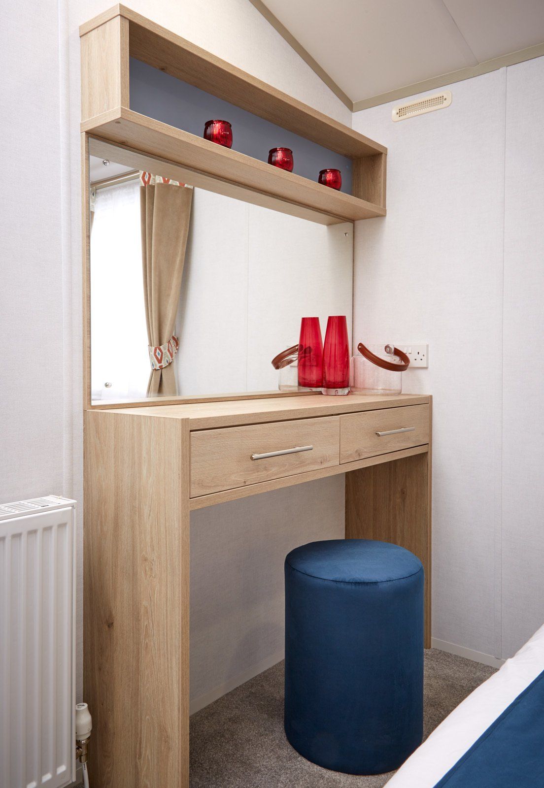 A bedroom with a vanity , mirror and ottoman.
