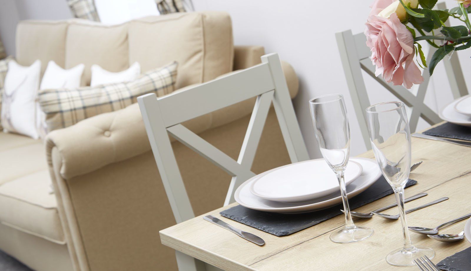 A table with plates , glasses , silverware and a vase of flowers on it in a living room.
