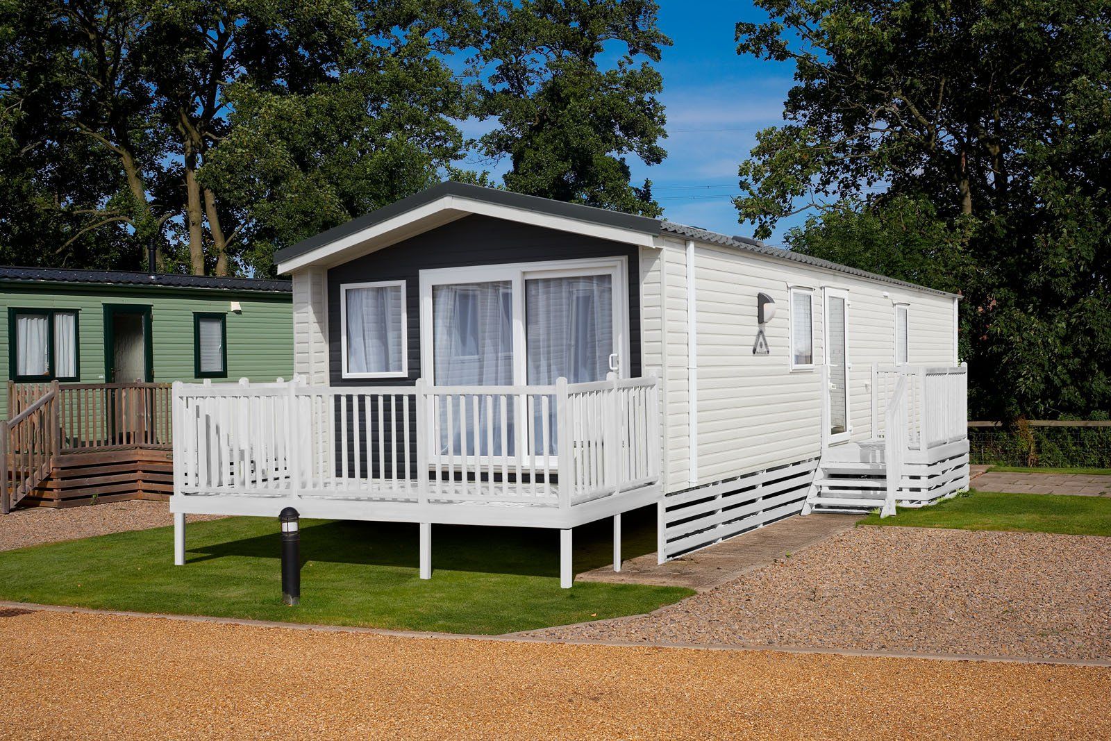 A mobile home with a large deck is sitting on top of a lush green field.