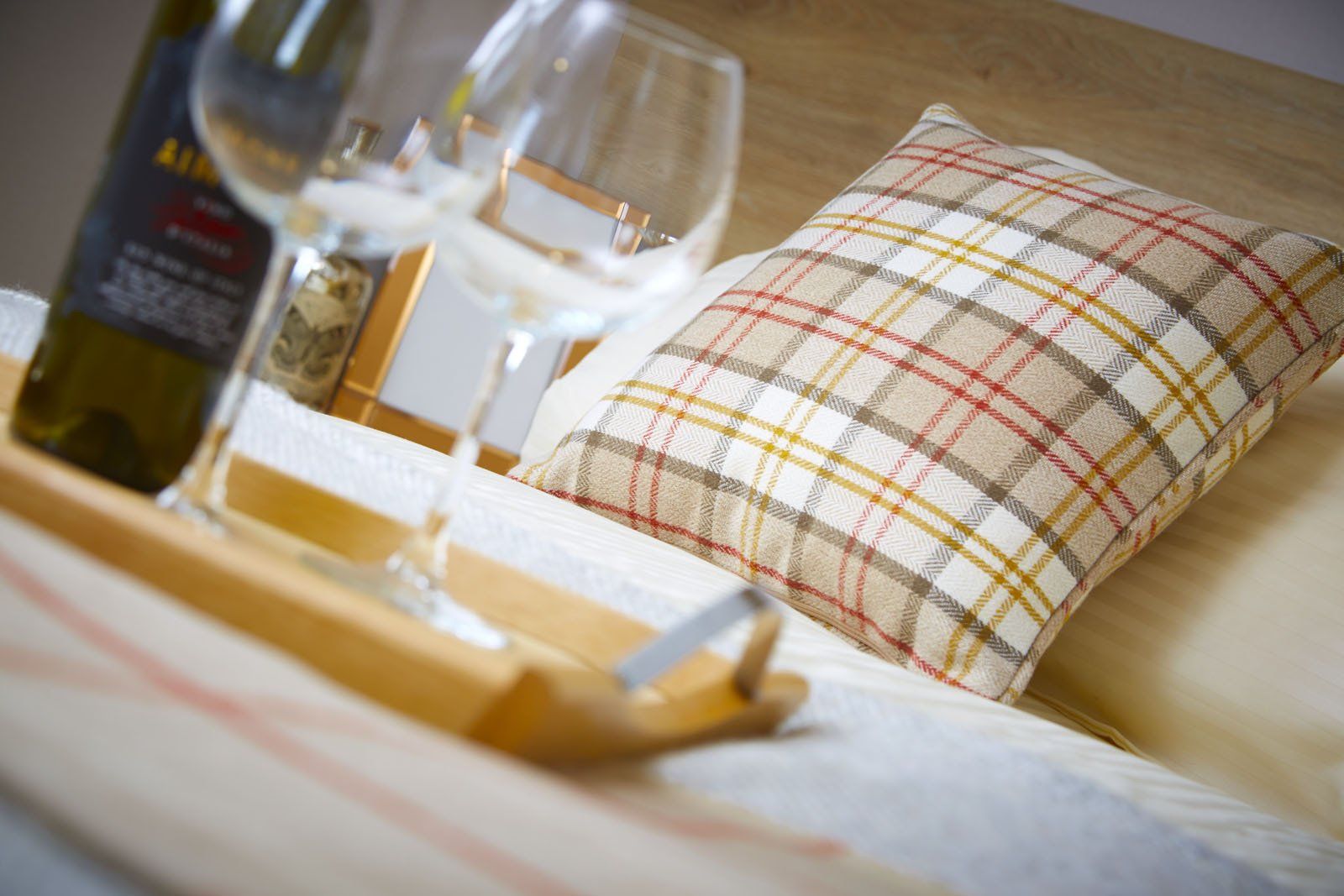 A bed with a pillow , wine glasses , and a bottle of wine.