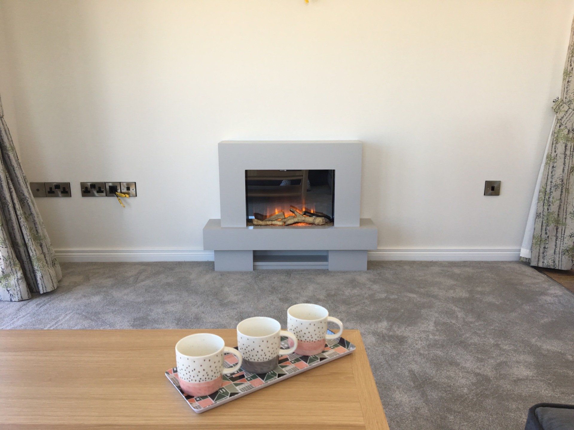 A living room with a fireplace and coffee cups on a table.