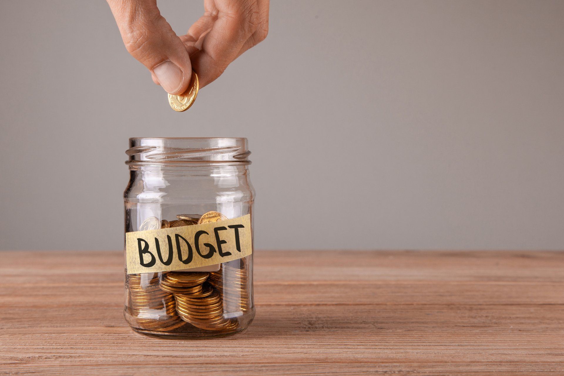 A person dropping a penny into a jar labeled budget