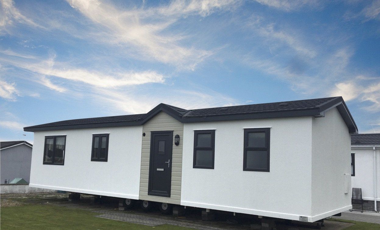 A white mobile home with a black roof is parked in a grassy field.