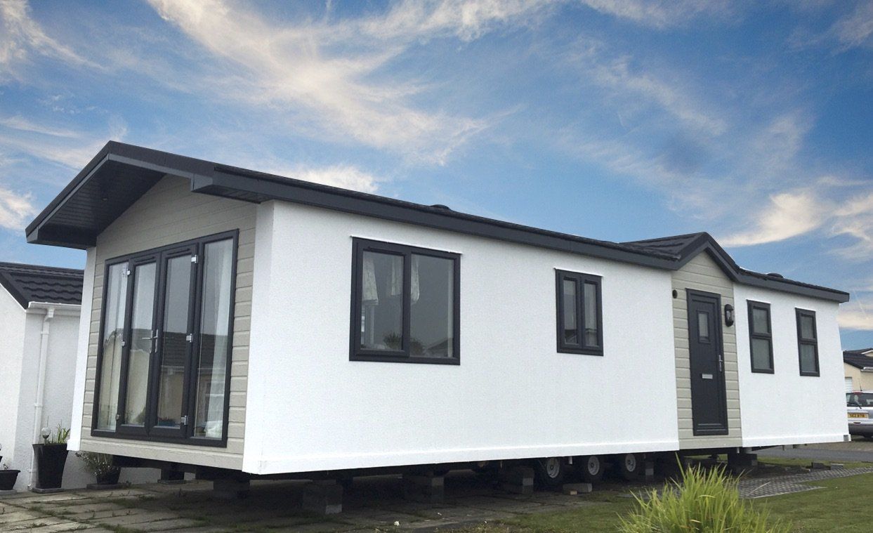 A white mobile home with black windows and a blue sky in the background.