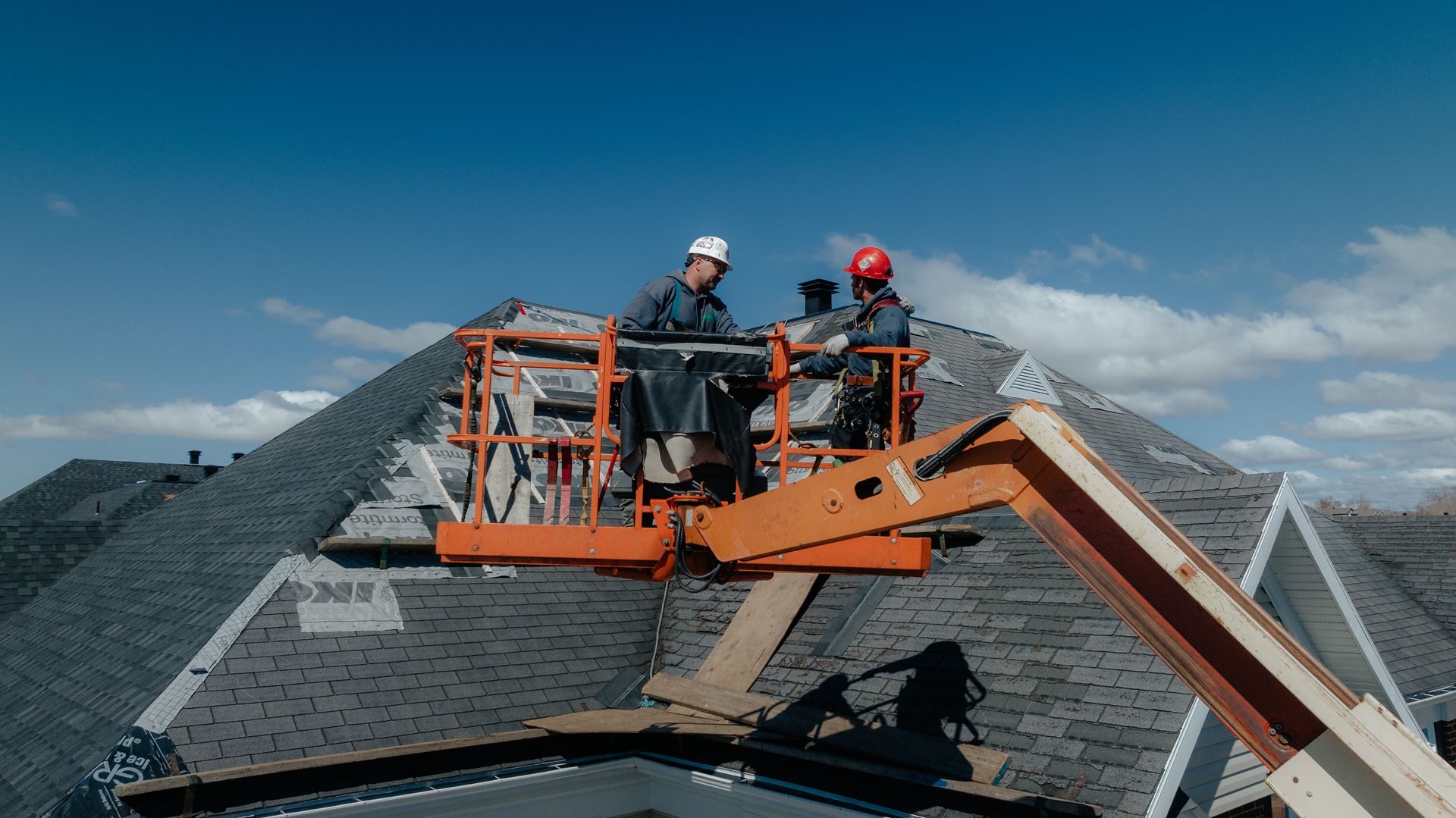 Deux couvreurs dans un ascenseur sur un toit, travaillant sur le toit sous un ciel bleu.