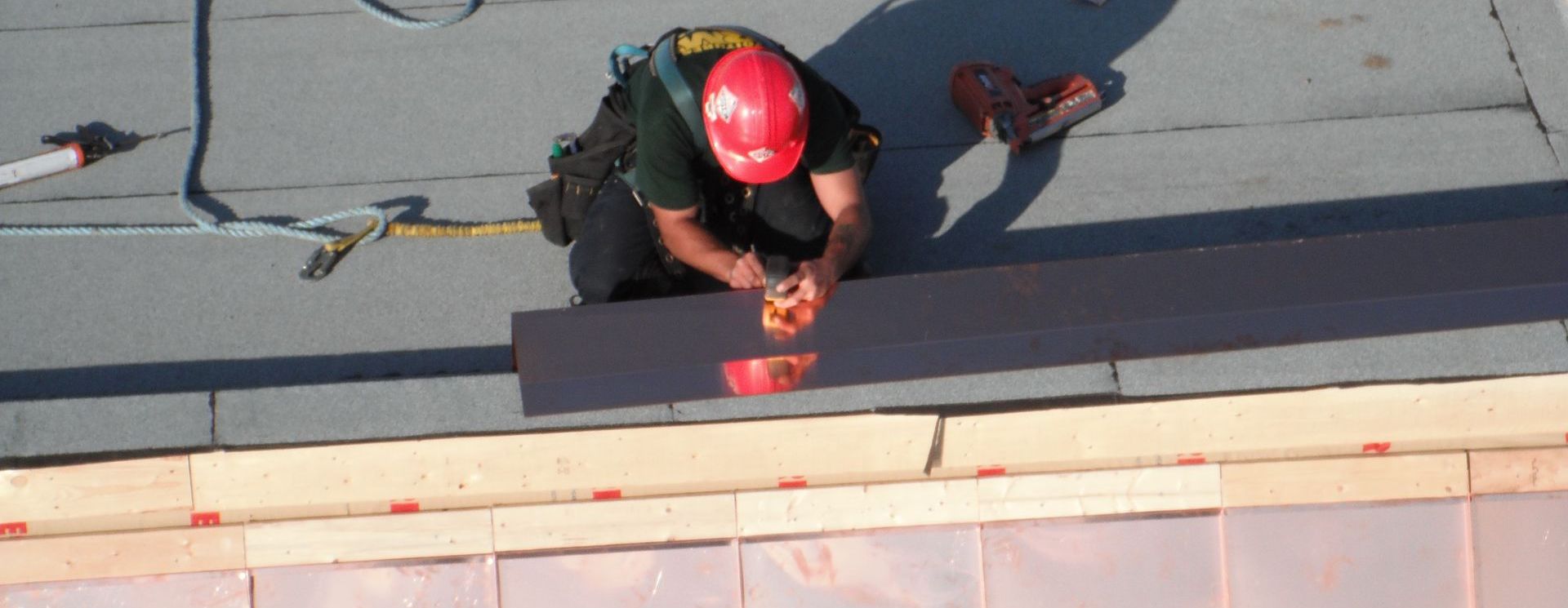 Un homme portant un casque rouge travaille sur un toit.
