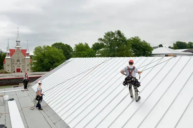 Un groupe de personnes travaille sur un toit avec une église en arrière-plan.