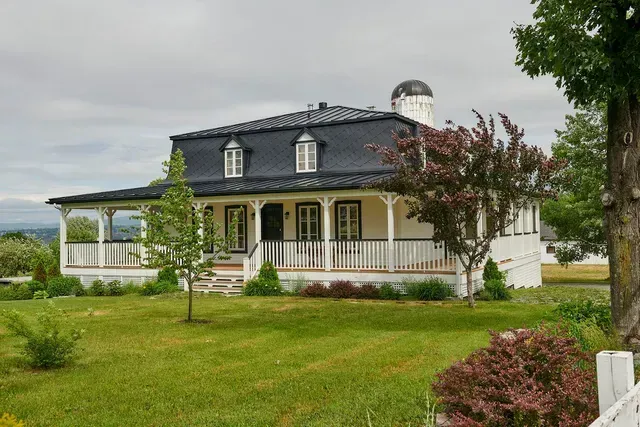 Une grande maison blanche avec un toit noir et un porche