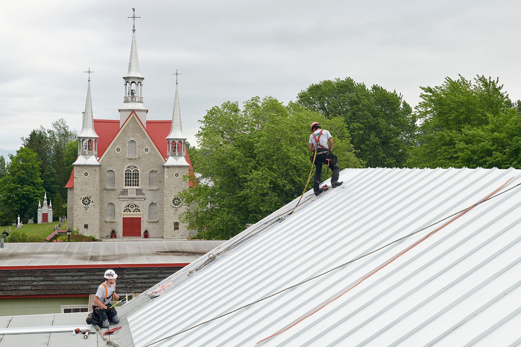Deux hommes travaillent sur le toit d'un immeuble avec une église en arrière-plan.