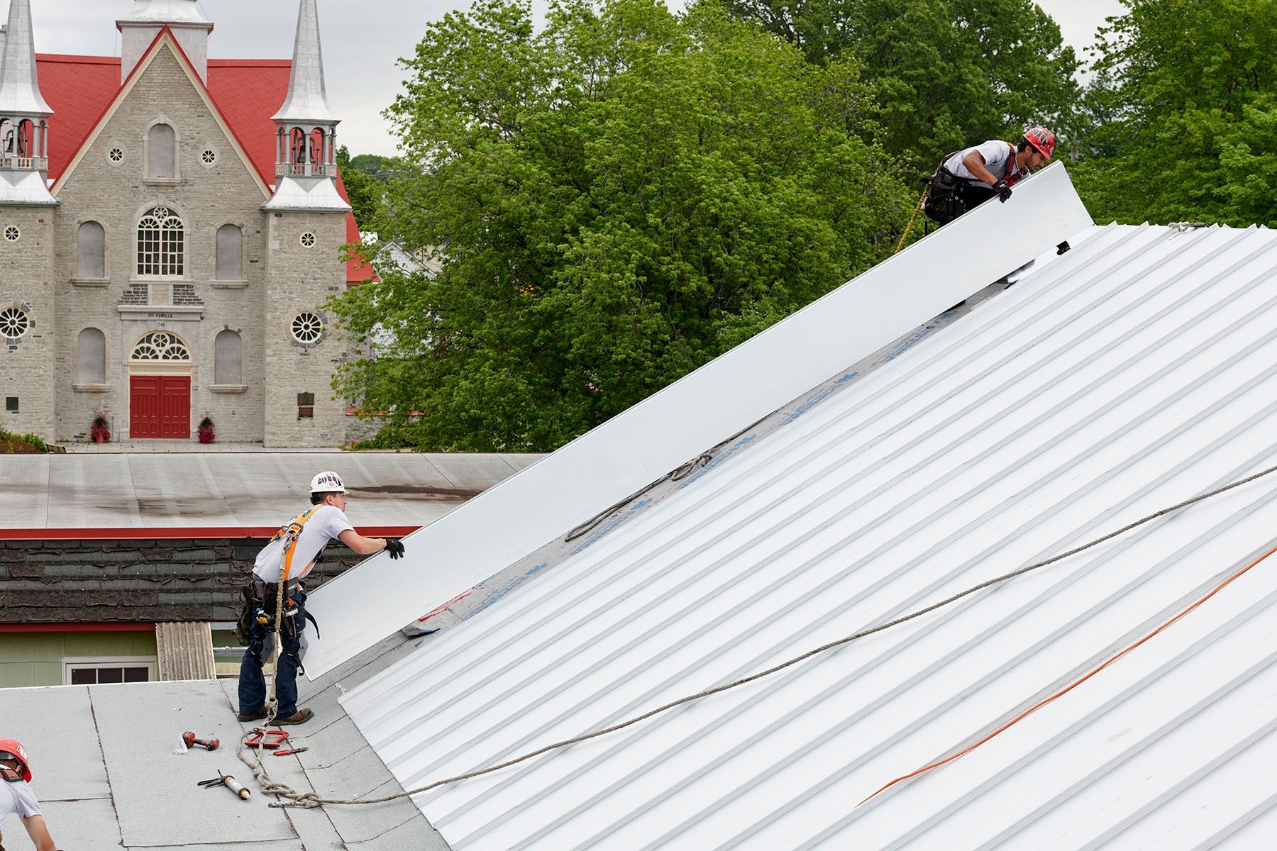 Deux hommes travaillent sur un toit avec une église en arrière-plan.