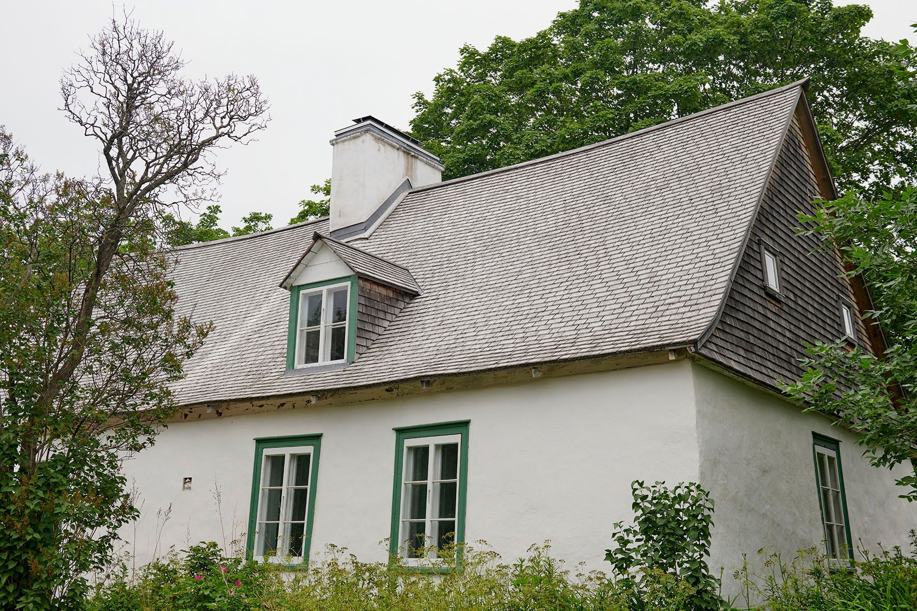 Une maison blanche avec un toit gris et des fenêtres vertes