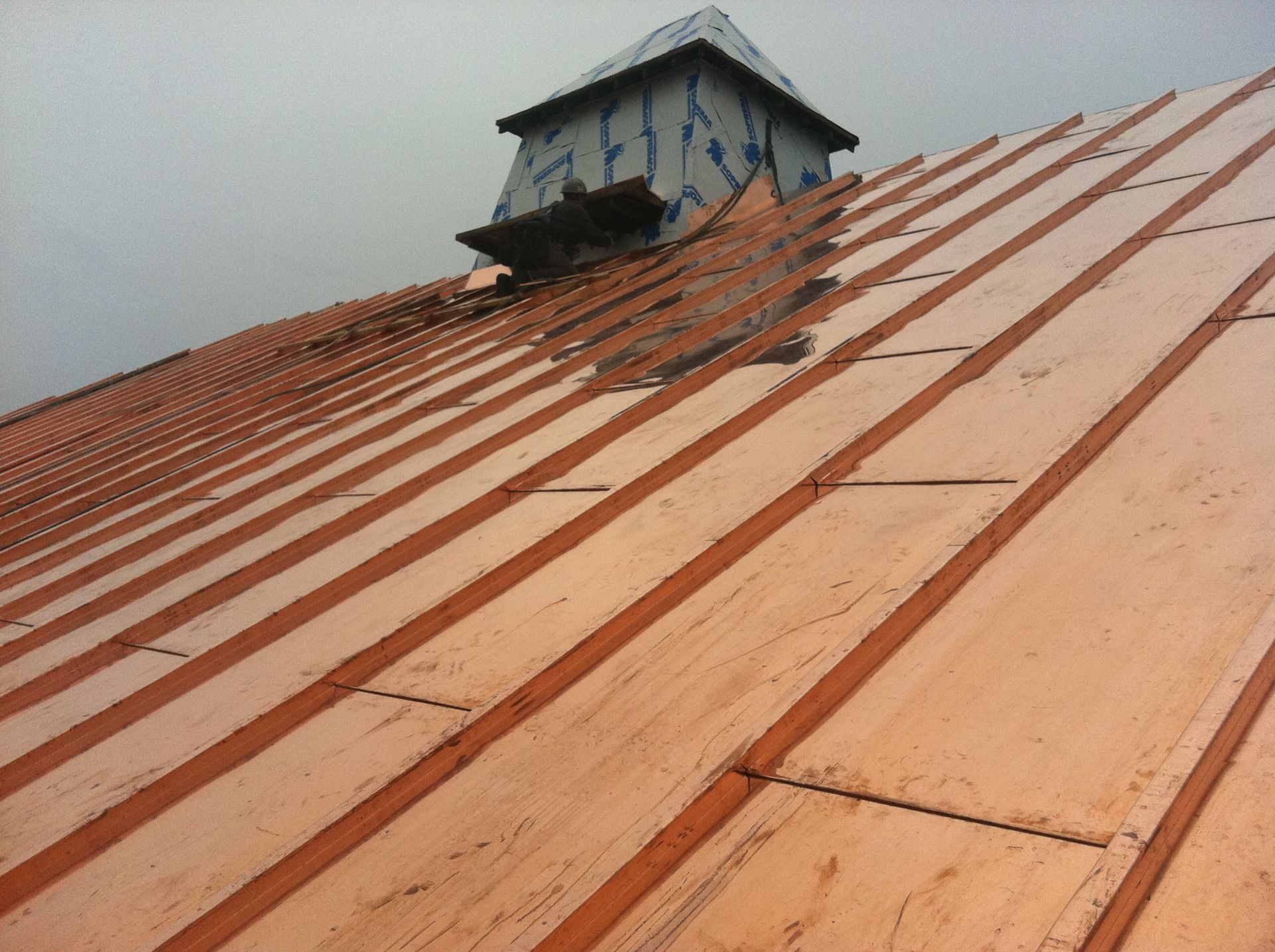 Toiture en cuivre avec une petite coupole carrée. Revêtement et solins métalliques, sous un ciel nuageux.