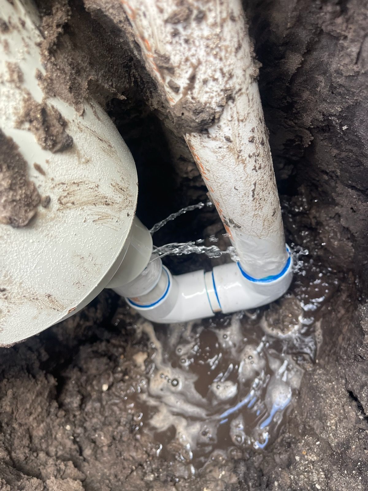 A broken PVC pipe connection leaks water into the soil.