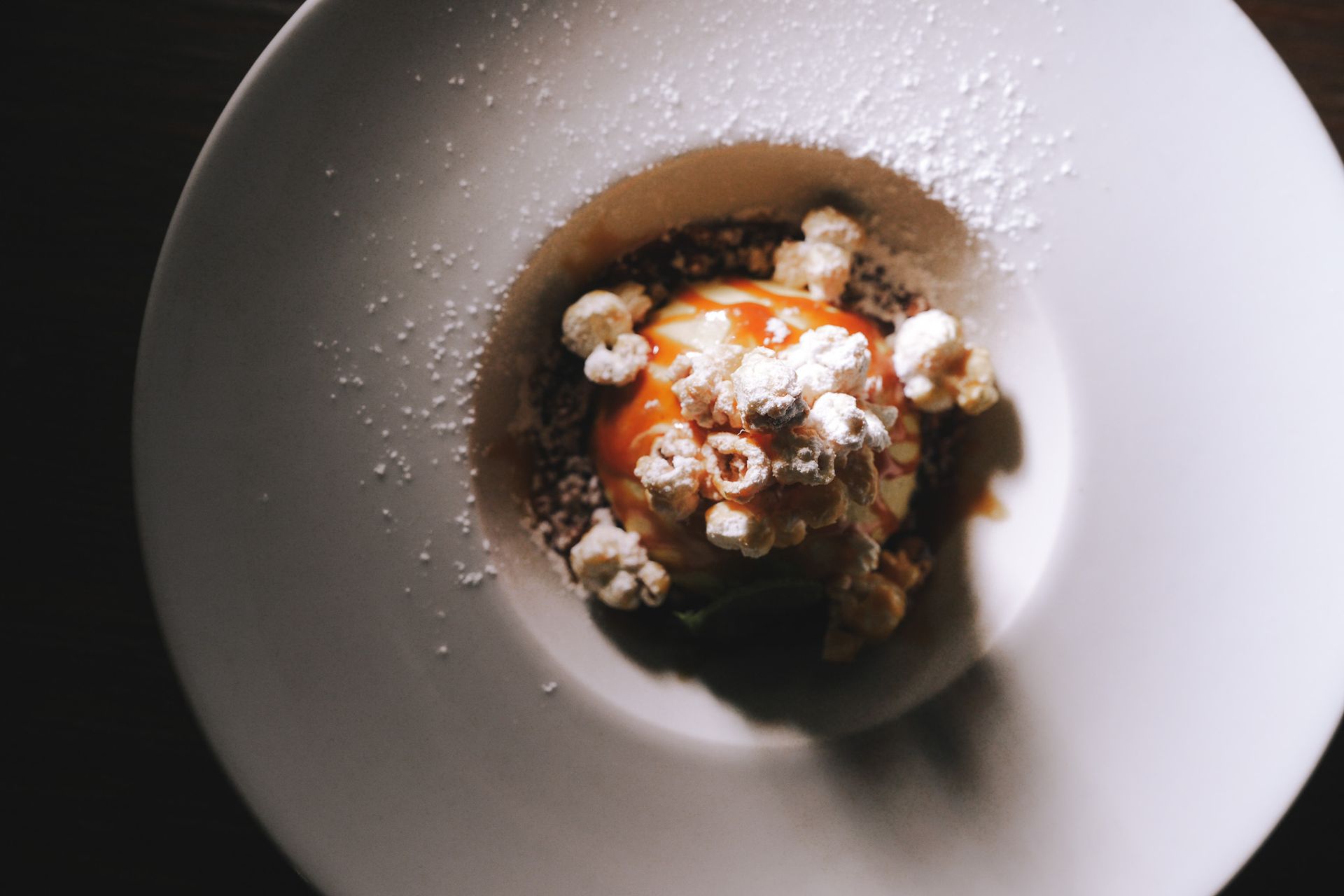 Dessert in una ciotola bianca: gelato con glassa al caramello, popcorn e zucchero a velo.