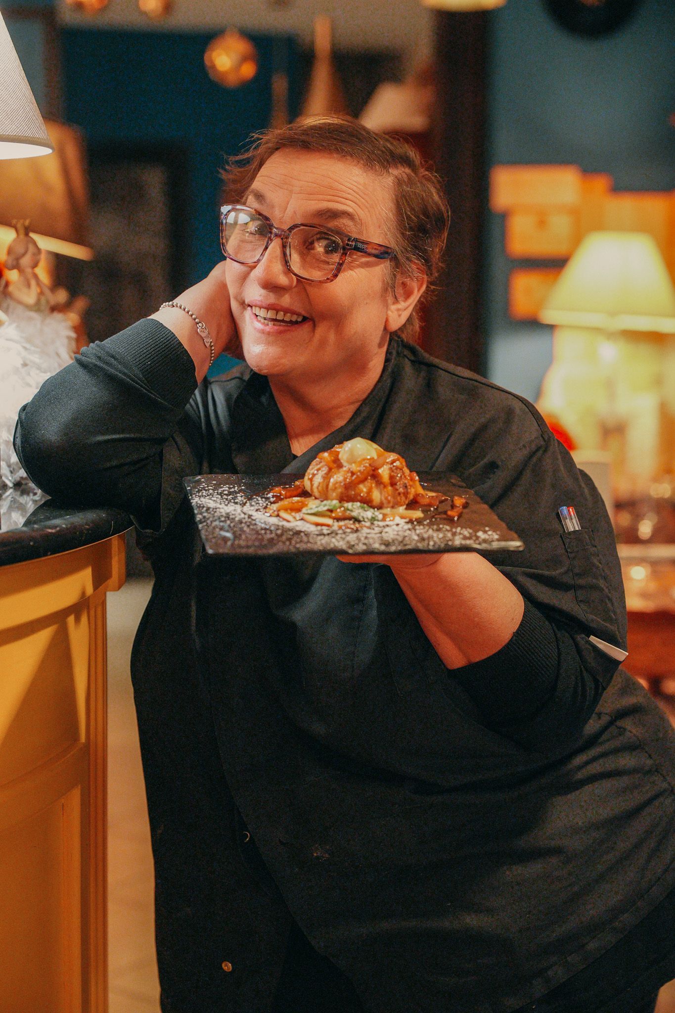 Donna sorridente con gli occhiali e un dolce su un piatto nero.