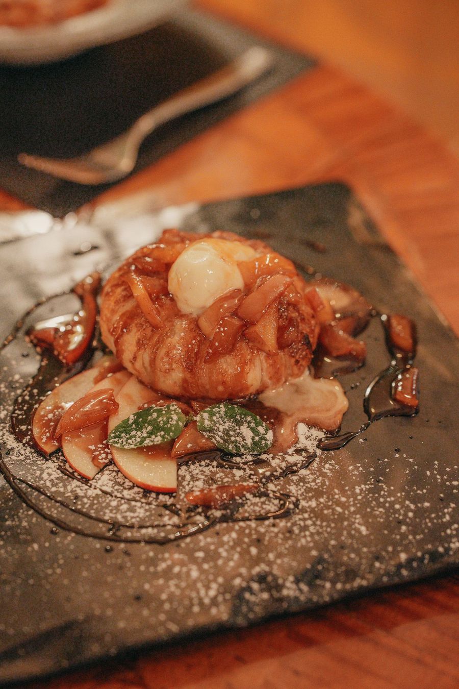 Dessert di mele su ardesia nera con glassa, zucchero a velo e menta.