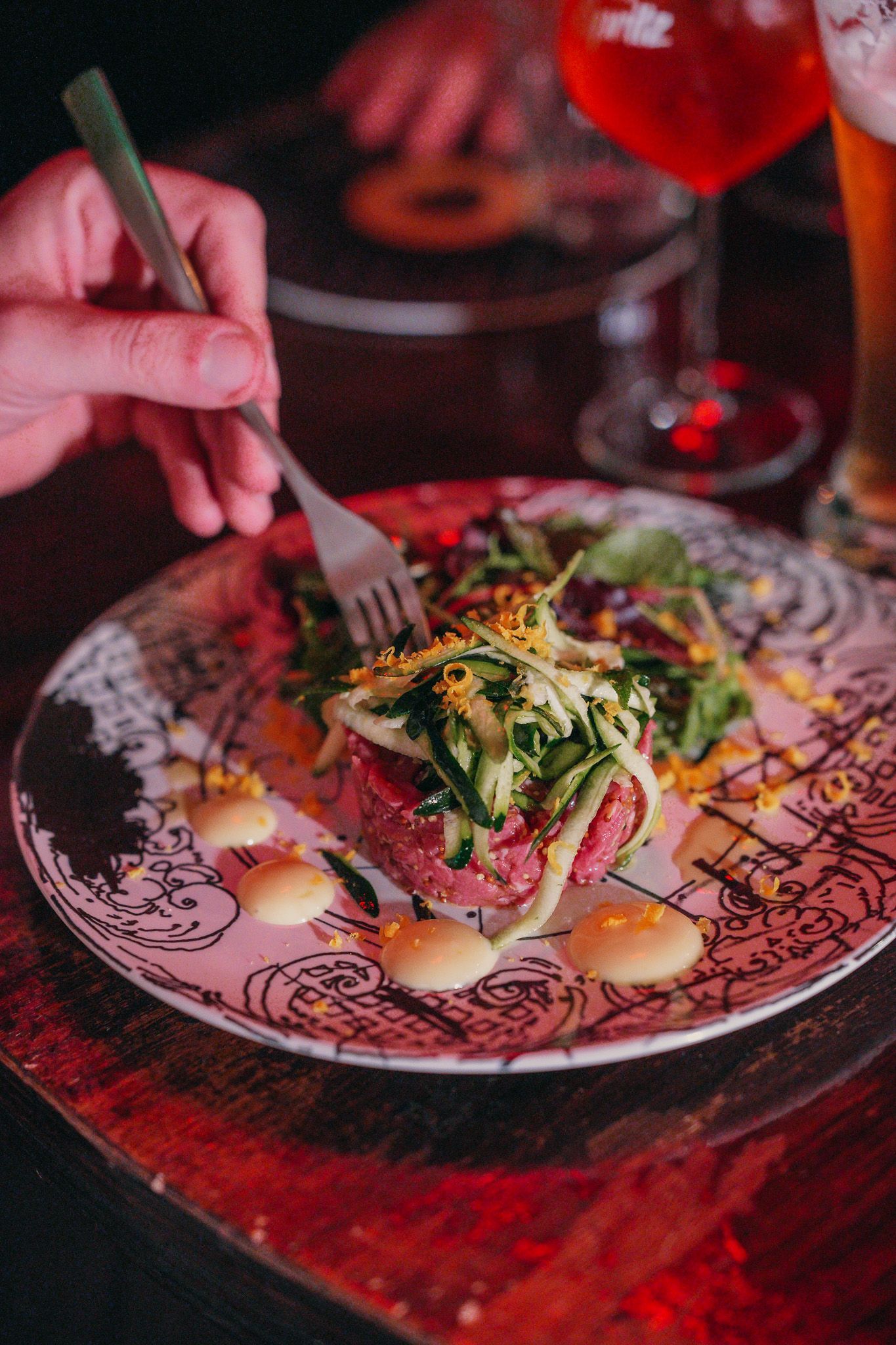 Persona che mangia un piatto di cibo con una forchetta. Il piatto contiene salsa e verdure. Luce rossa.