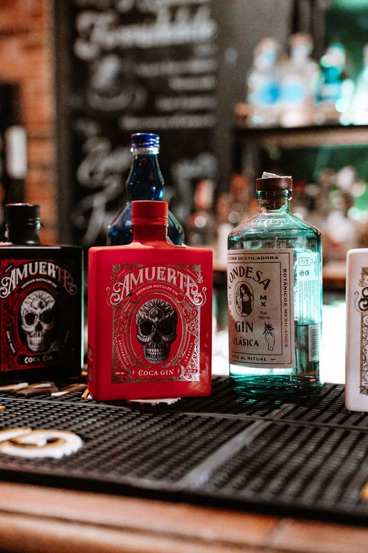 Bottiglie di liquore su un bancone: bottiglie rosse, blu e verdi con teschio e altre etichette.