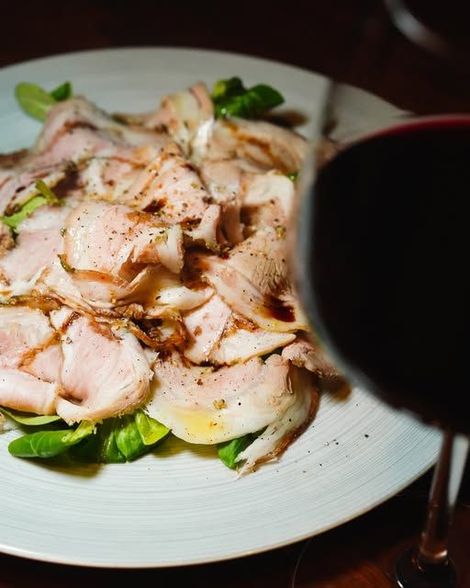 Piatto di carne affettata su un piatto, con un bicchiere di vino rosso in primo piano.