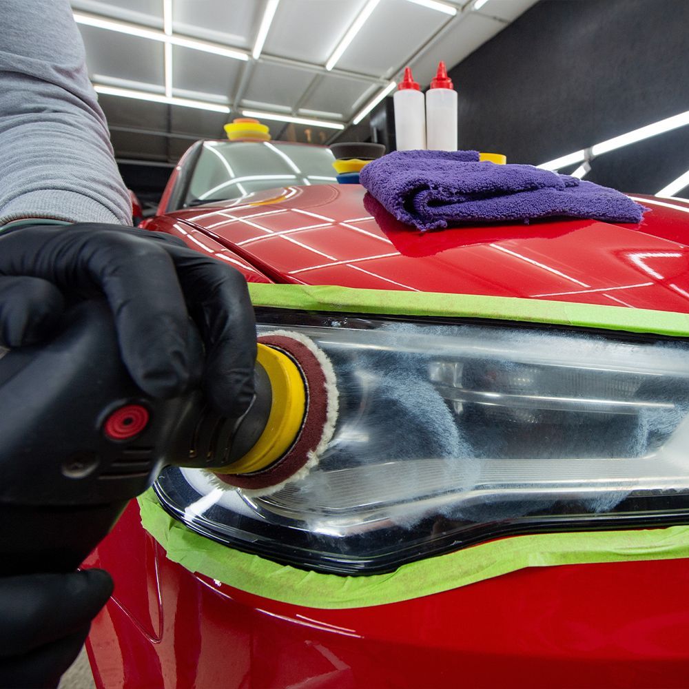 A person is polishing the headlights of a red car.