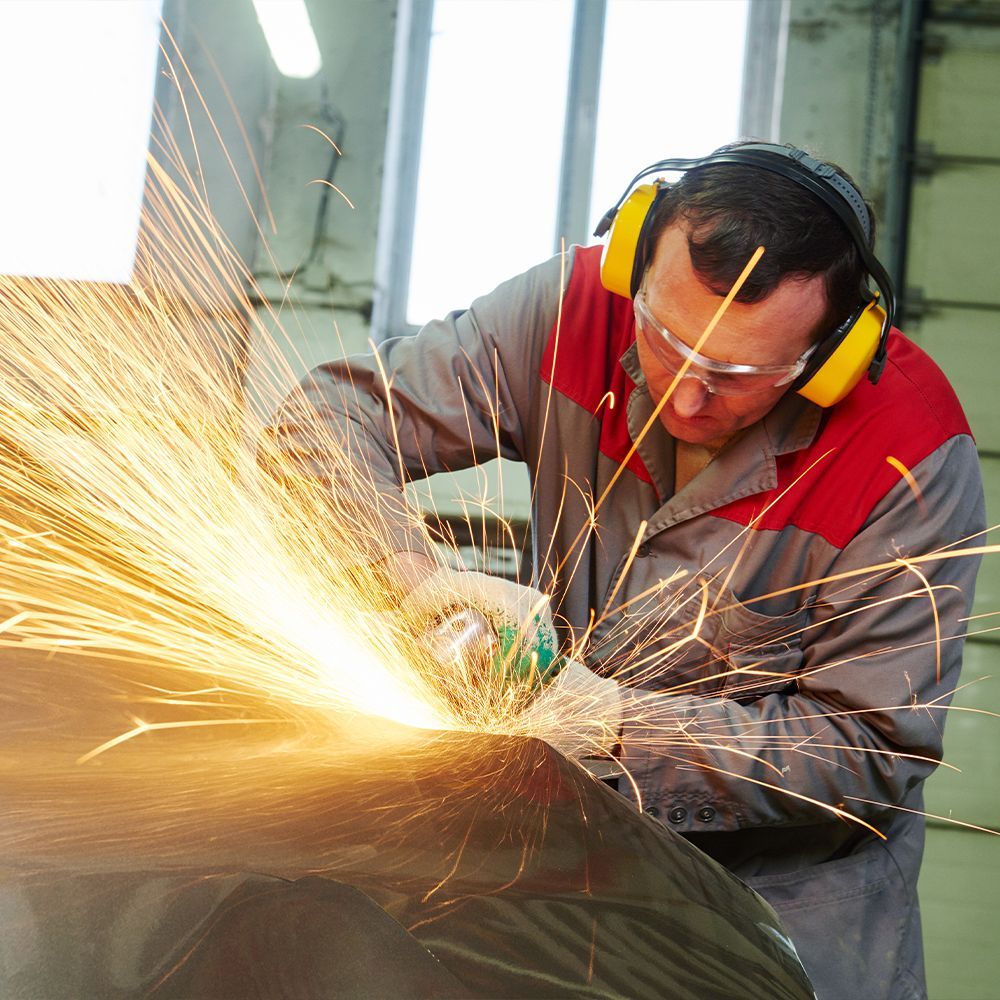 A man wearing ear defenders is grinding a piece of metal
