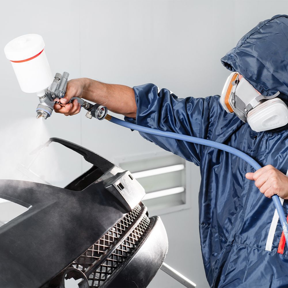 A man wearing a mask is spray painting a car bumper.