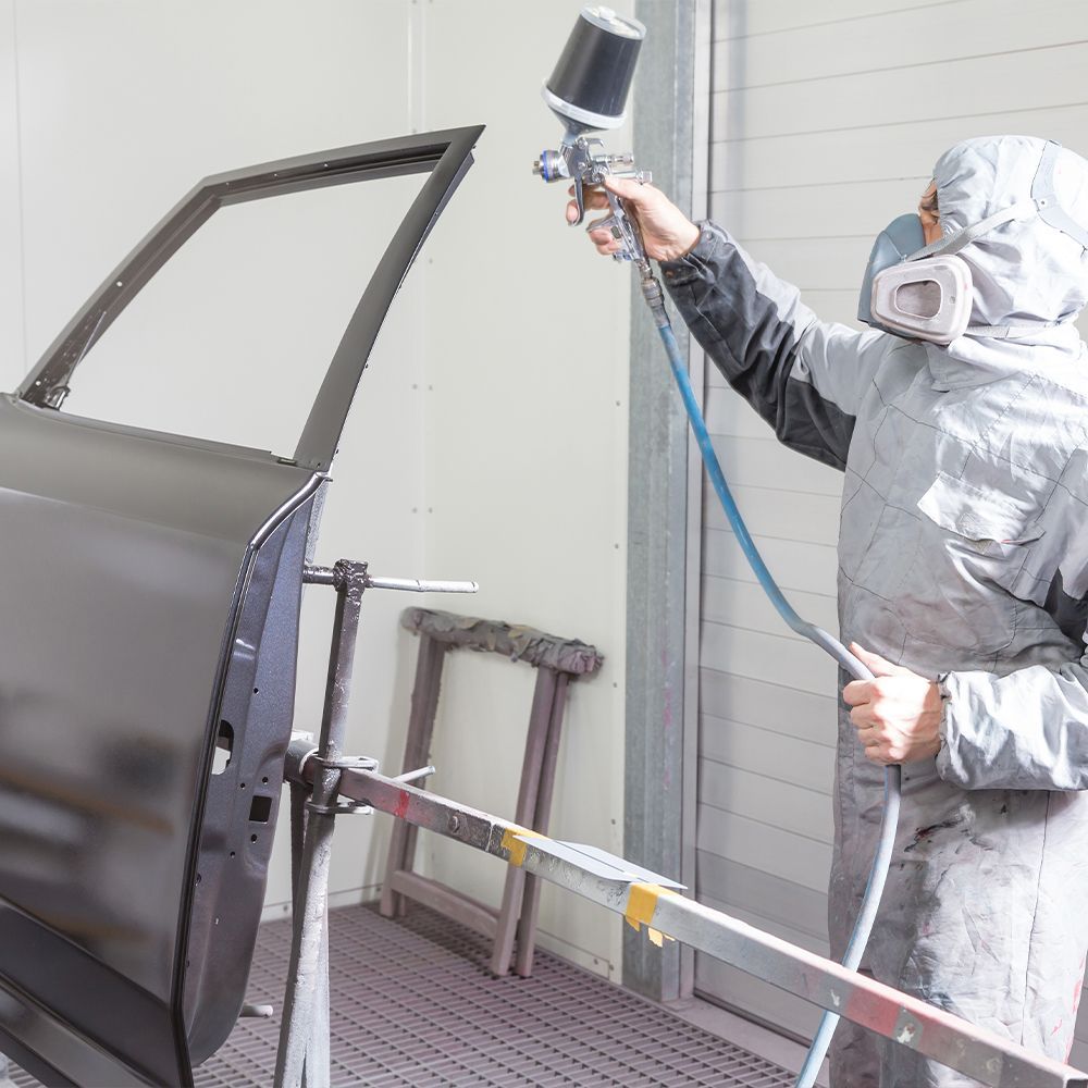 A man is spray painting a car door in a garage
