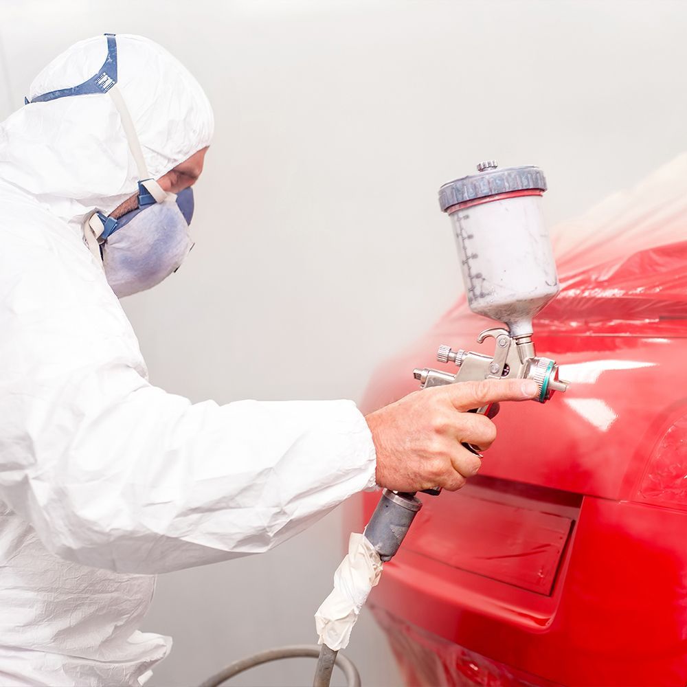 A man in a protective suit is spray painting a red car.