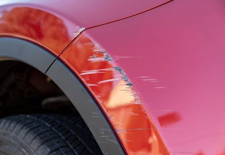 A close up of a red car with a scratch on the fender.