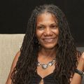 A woman with dreadlocks and a necklace smiles for the camera