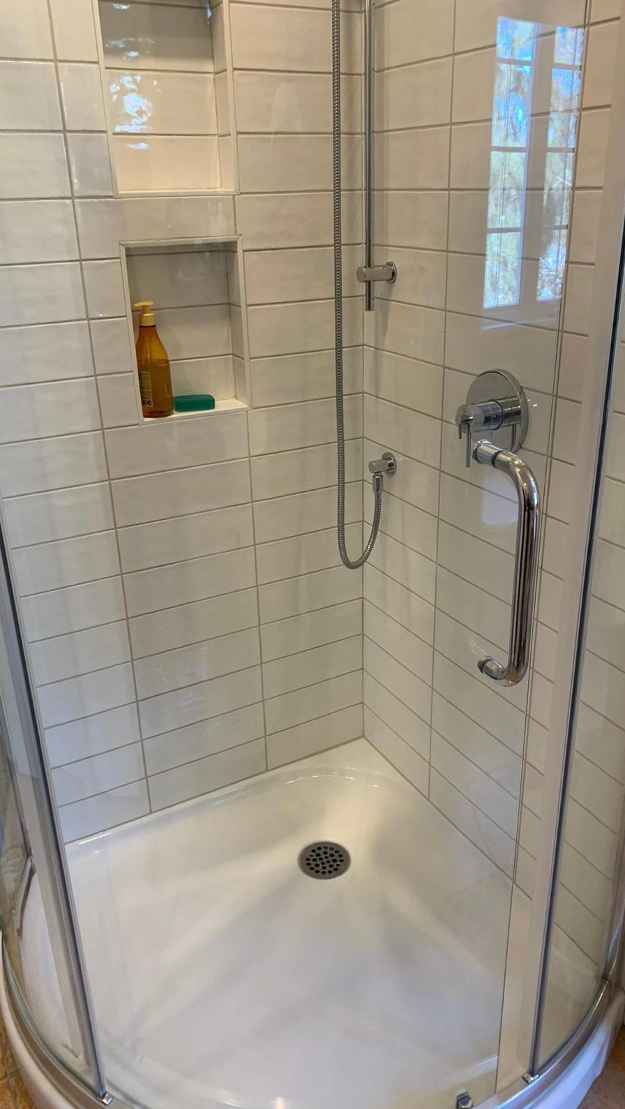 Une cabine de douche dans une salle de bains avec carrelage blanc et porte vitrée.
