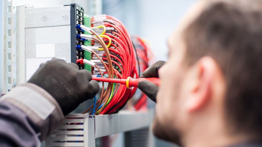 Electrician in Black Gloves Using a Screwdriver on A Panel of Colourful Wires — A & J Electrical Contractors in Tamworth, NSW