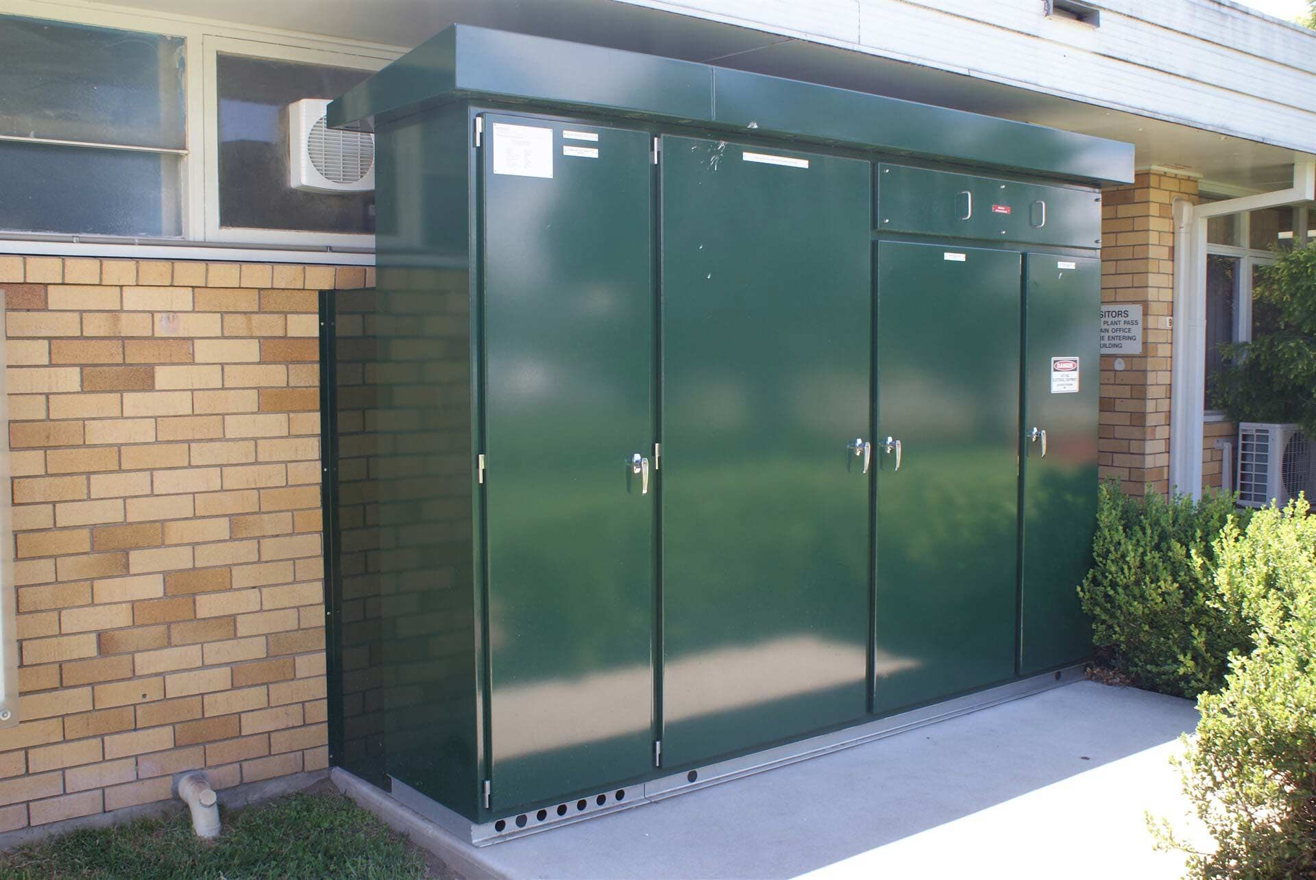 A Brick Building with A Green Cabinet in Front of It — A & J Electrical Contractors in Taminda, NSW