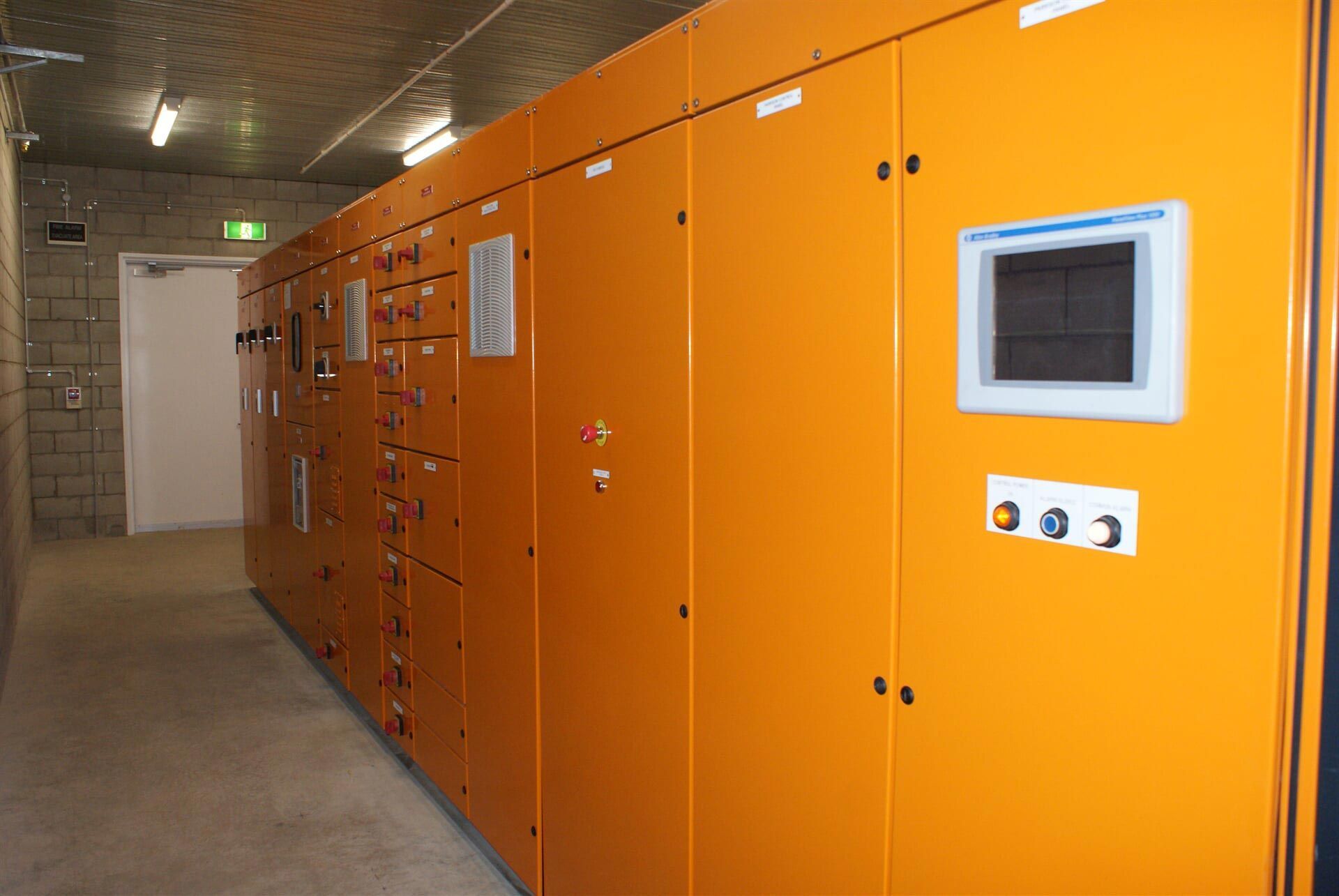 A Row of Orange Electrical Boxes in A Room with A Monitor on The Wall — A & J Electrical Contractors in Taminda, NSW