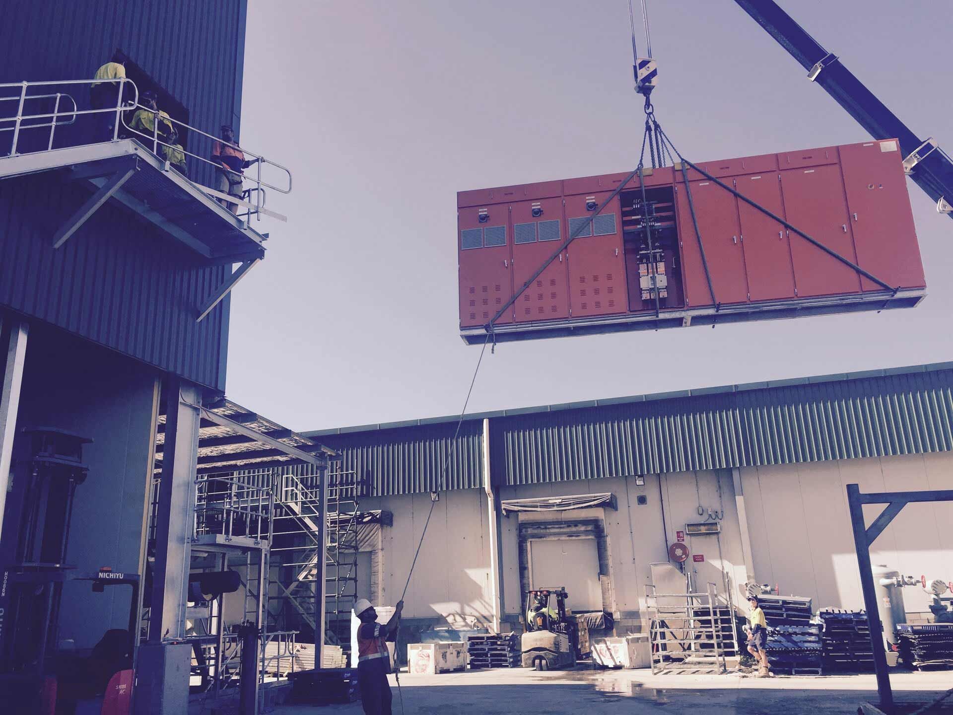 A Large Red Box Is Being Lifted by A Crane in Front of A Building — A & J Electrical Contractors in Taminda, NSW