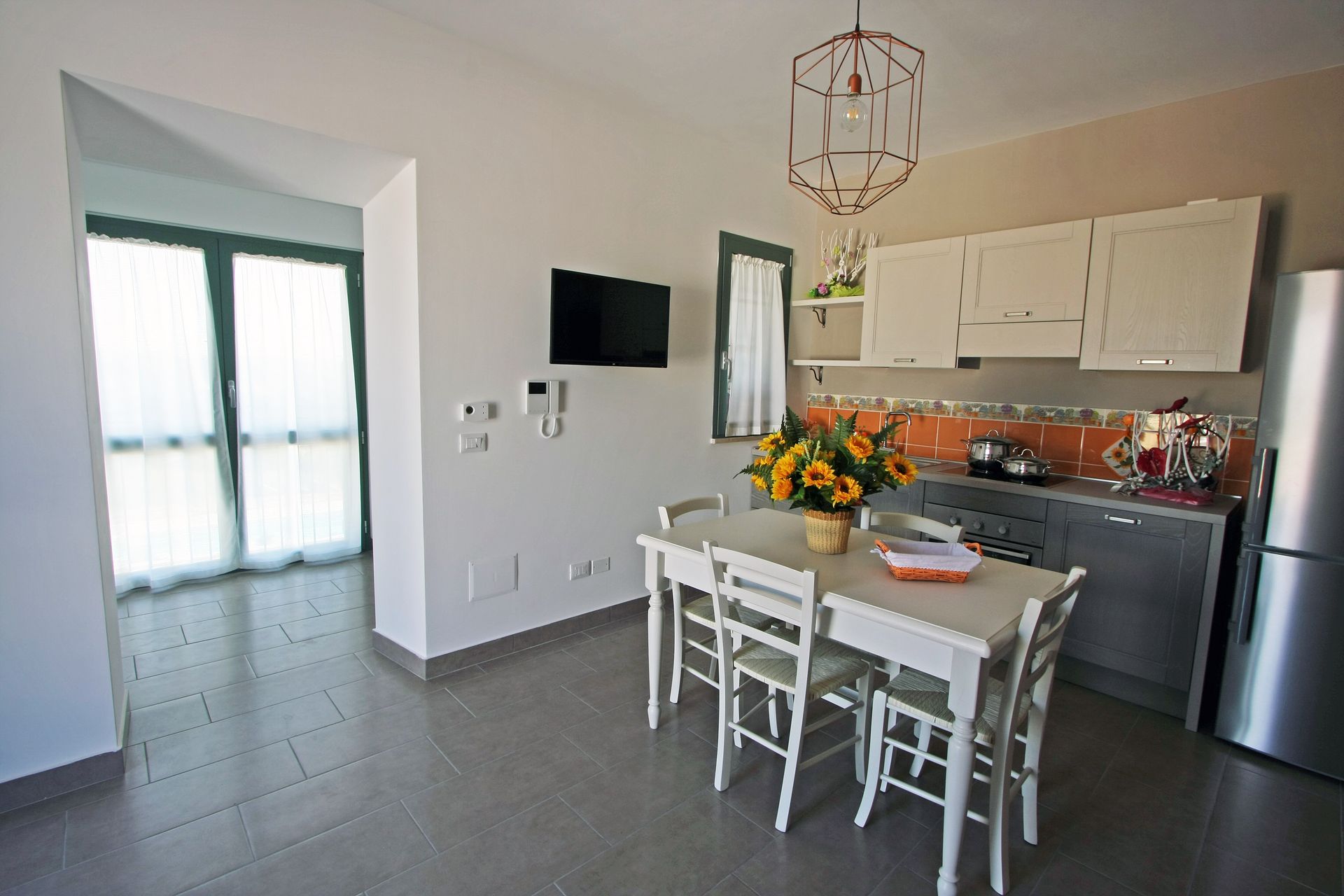 In una stanza luminosa, accanto a una cucina con mobili grigi e un frigorifero i