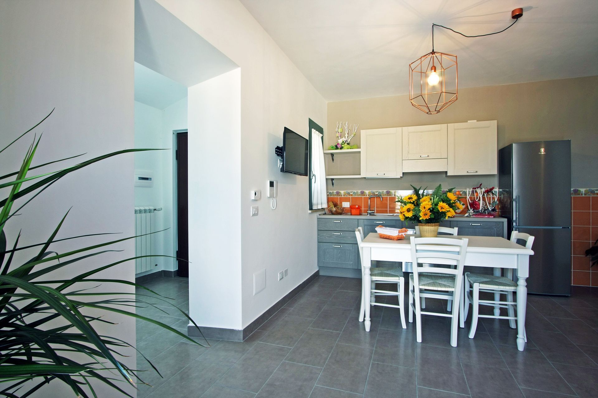 Una cucina con zona pranzo, arredata con tavolo e sedie bianchi, frigorifero in acciaio inox e pensili chiari.