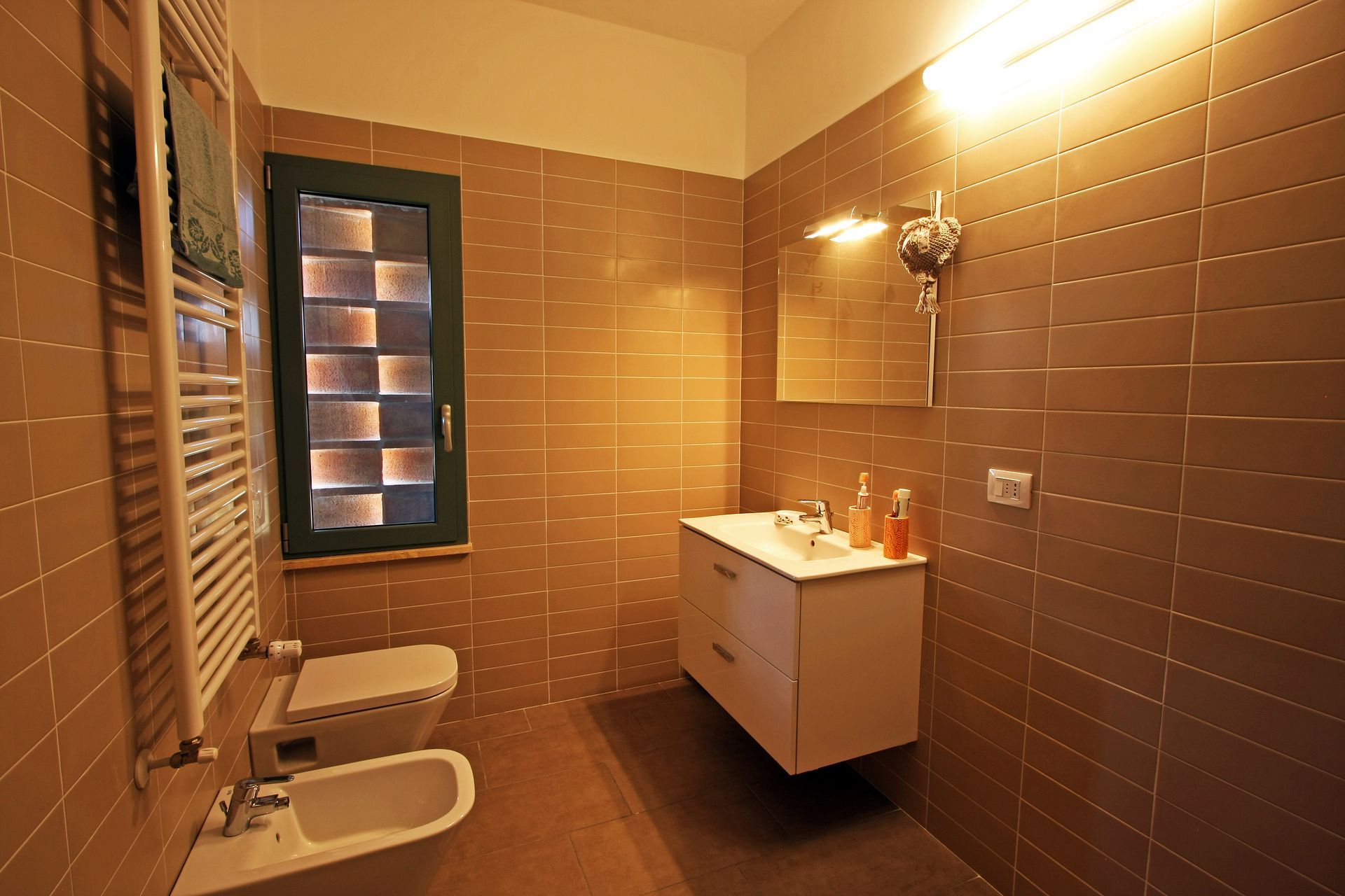 Un bagno moderno con pareti rivestite di piastrelle marroni, un mobile lavabo bianco, un WC